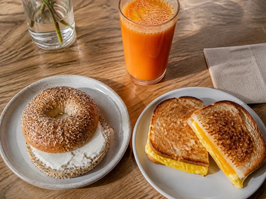 A breakfast spread of bagels, spreads and juice on a wooden table.
