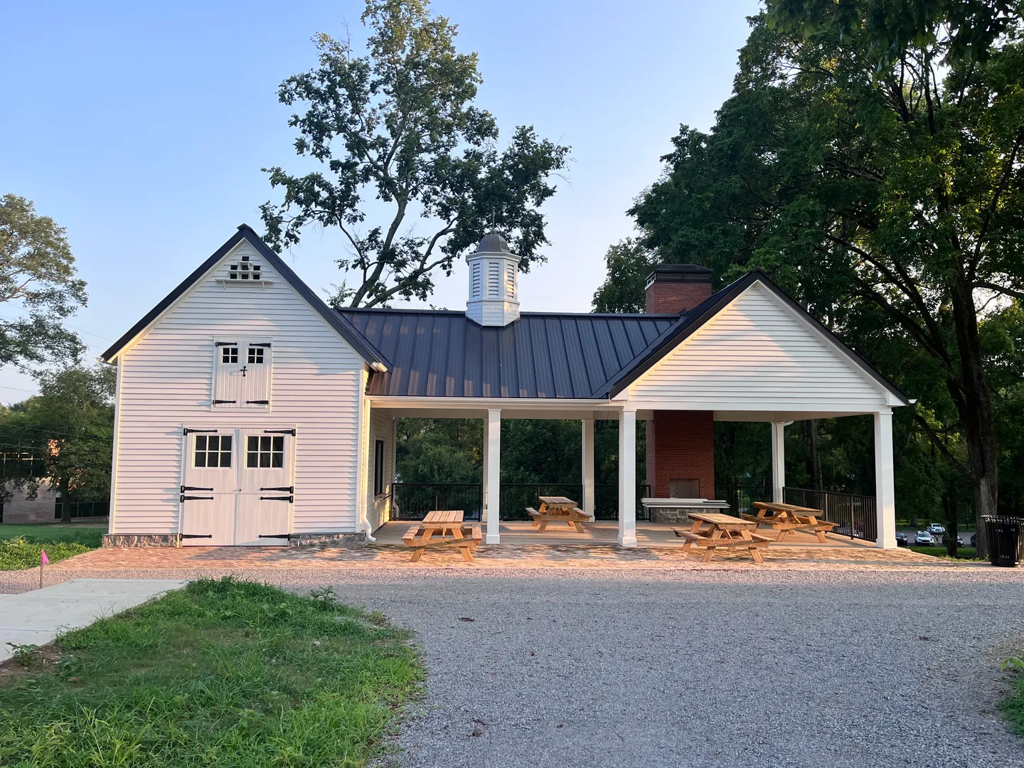 The Sunnyside pavilion at golden hour — a white barn with a black metal roof and cupola, open on one side to picnic tables and a brick fireplace.